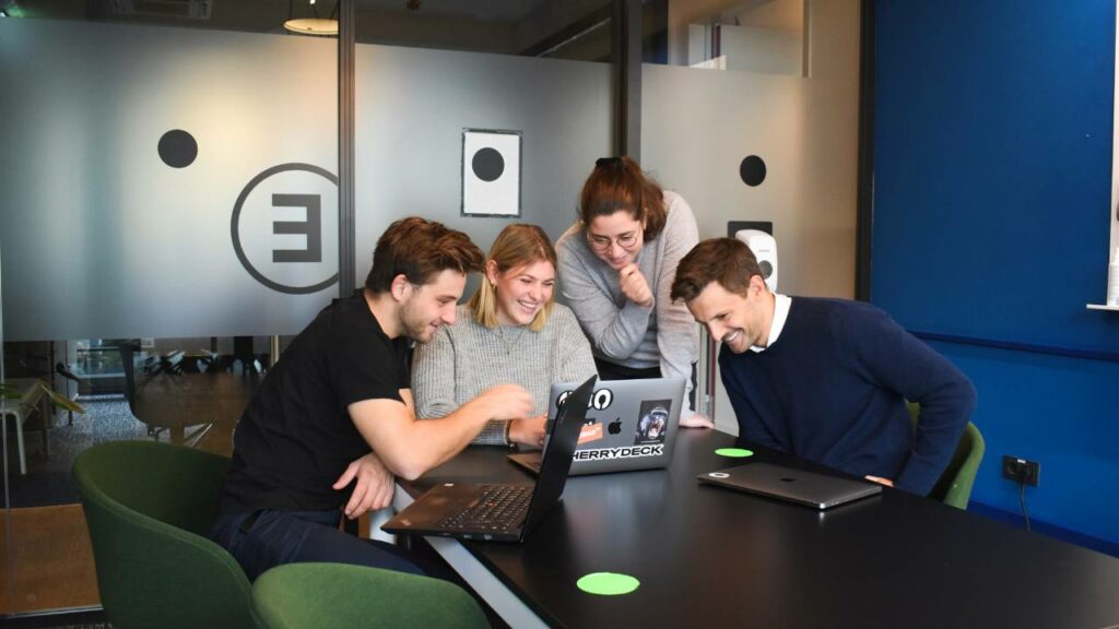A group of happy employees looking at a laptop and laughing together 