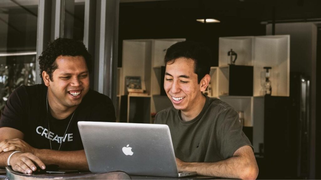 Two employees smiling while using an Apple laptop