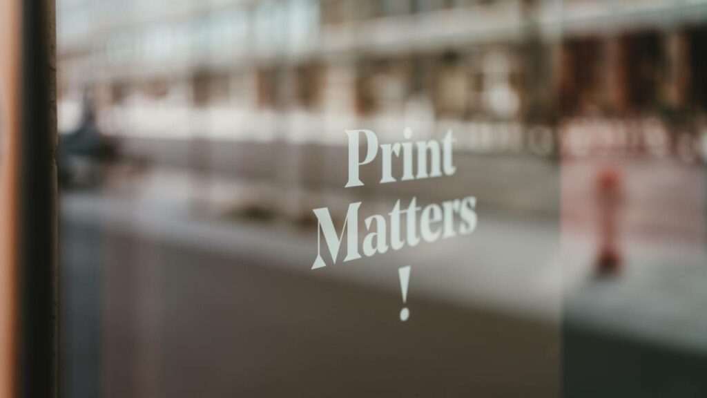 A photo of a Print Matters sign seen through a window